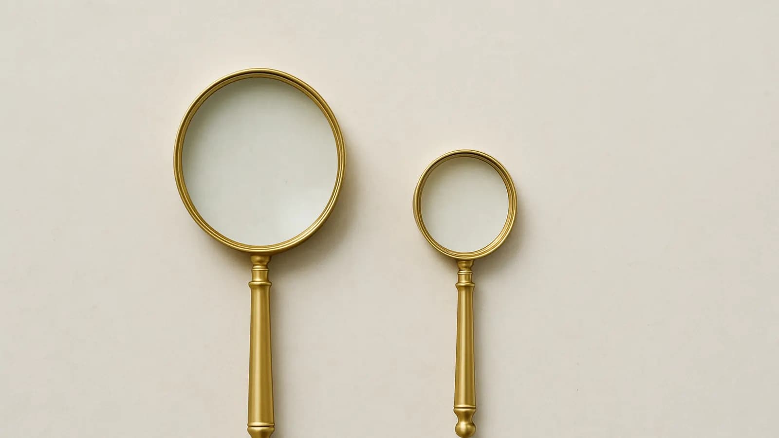 Two brass magnifying glasses of different sizes lying side by side on a pale stone surface.
