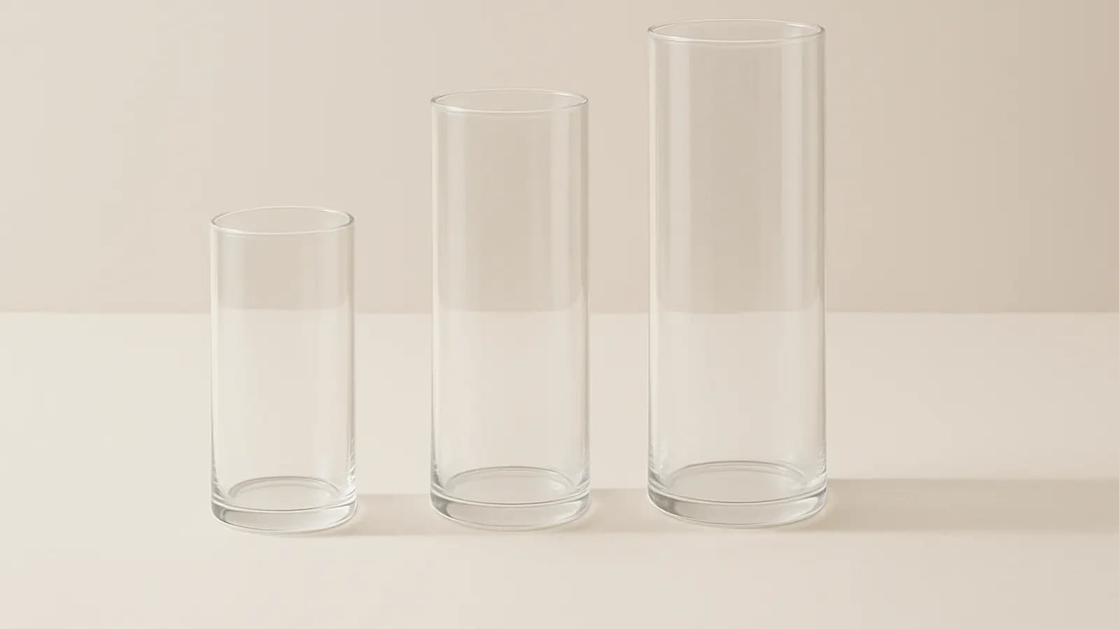 Three plain glass cylinders of increasing height standing side by side on a pale studio surface.